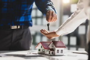 Remise de clés entre deux personnes avec une maquette de maison, illustrant un investissement immobilier sécurisé et accompagné par un expert-comptable.