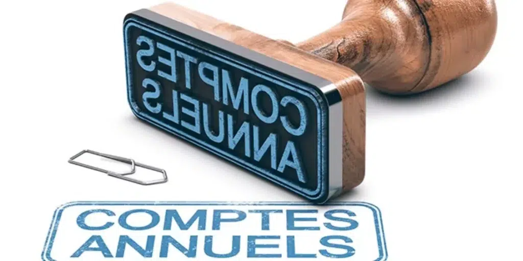 Tampon en bois avec l’inscription « COMPTES ANNUELS », posé à côté de son empreinte bleue sur une feuille blanche, symbolisant la validation des états financiers d’une entreprise.