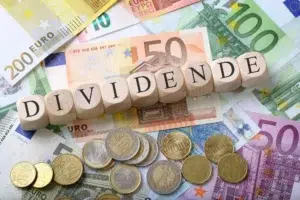 Image illustrant le concept de versement de dividendes, avec le mot « DIVIDENDE » inscrit sur des cubes en bois posés sur des billets et pièces en euros.
