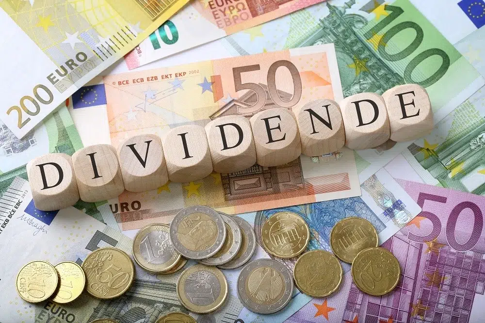 Image illustrant le concept de versement de dividendes, avec le mot « DIVIDENDE » inscrit sur des cubes en bois posés sur des billets et pièces en euros.
