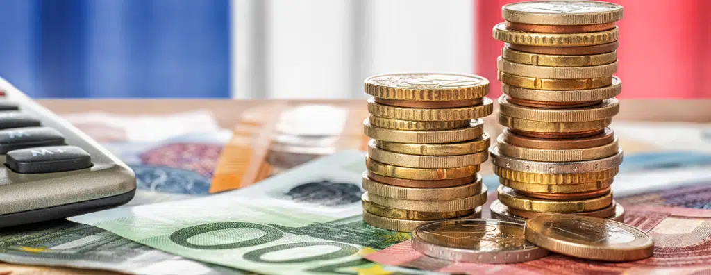 Pièces et billets en euros empilés devant un calculateur, illustration de la préparation du budget 2026 et du pilotage de trésorerie d’entreprise.