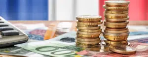 Pièces et billets en euros empilés devant un calculateur, illustration de la préparation du budget 2026 et du pilotage de trésorerie d’entreprise.